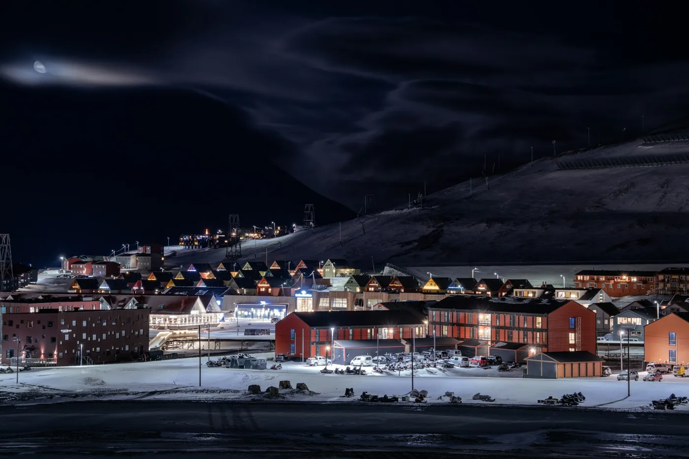 Beleuchtete Häuser von Longyearbyen unter einem dunklen, verschneiten Hang in der Polarnacht