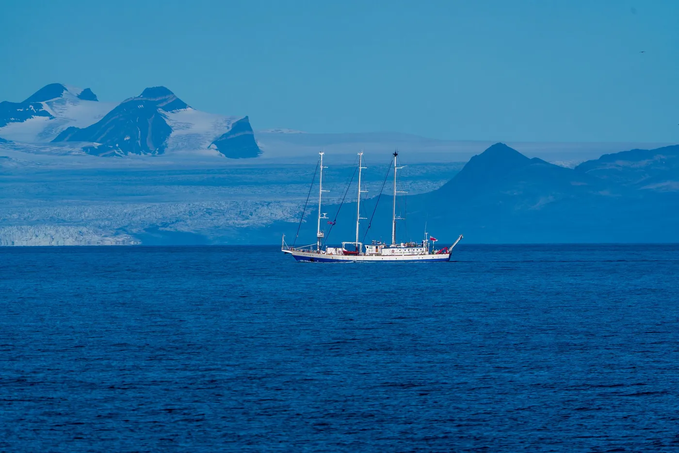Dreimastiges Segelschiff auf einem tiefblauen Fjord mit Gletscher und Bergen dahinter