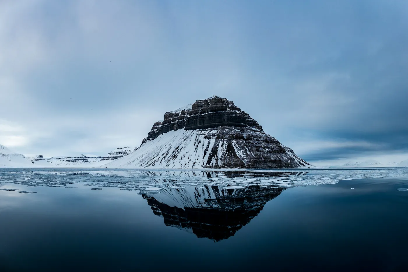Montagna a forma di piramide riflessa in acque calme con ghiaccio marino alla deriva