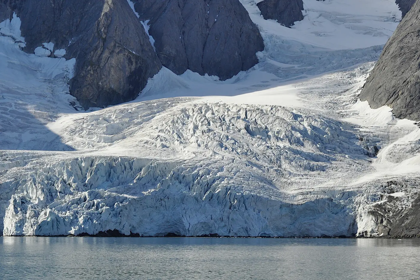 Lingua glaciale crepacciata che scende tra vette scure fino all'acqua