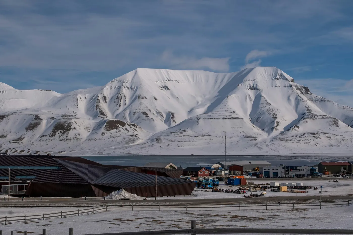 Un'ampia montagna innevata sopra i bassi edifici di Longyearbyen in una limpida giornata di fine inverno