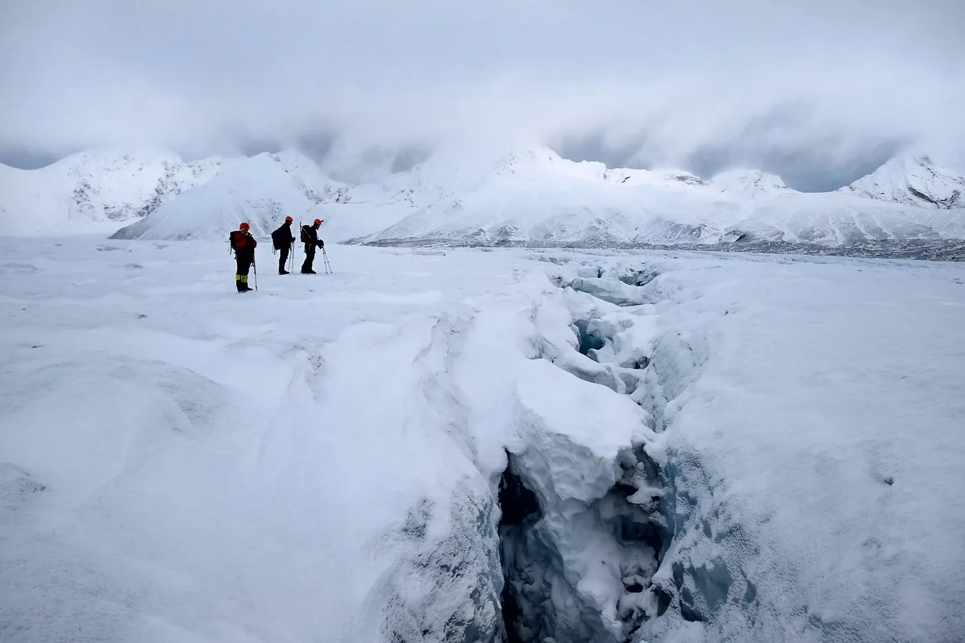 Drei Wanderer auf einem schneebedeckten Gletscher neben einer tiefen Gletscherspalte, die Berge in Wolken