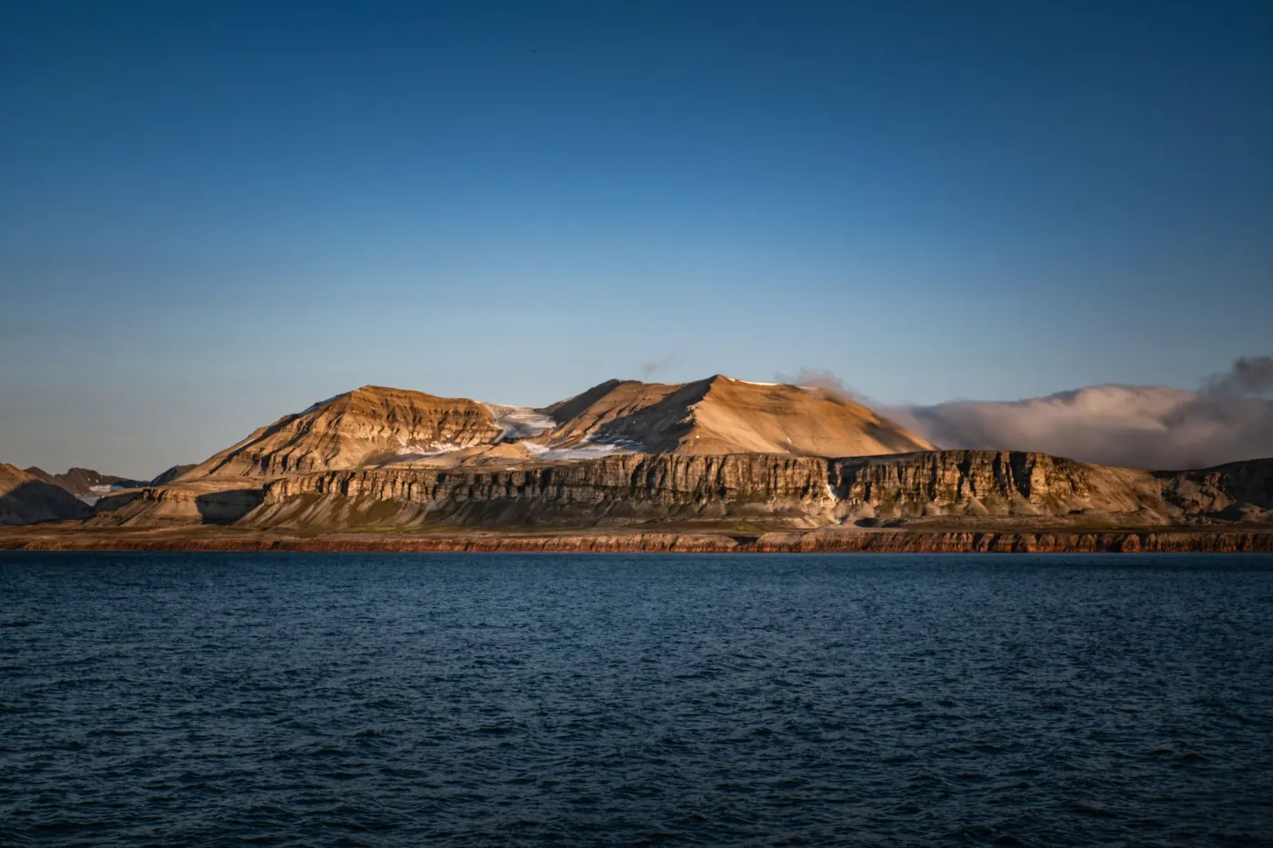 Montagnes à sommet plat baignées d’une lumière dorée rasante au-dessus d’une mer sombre