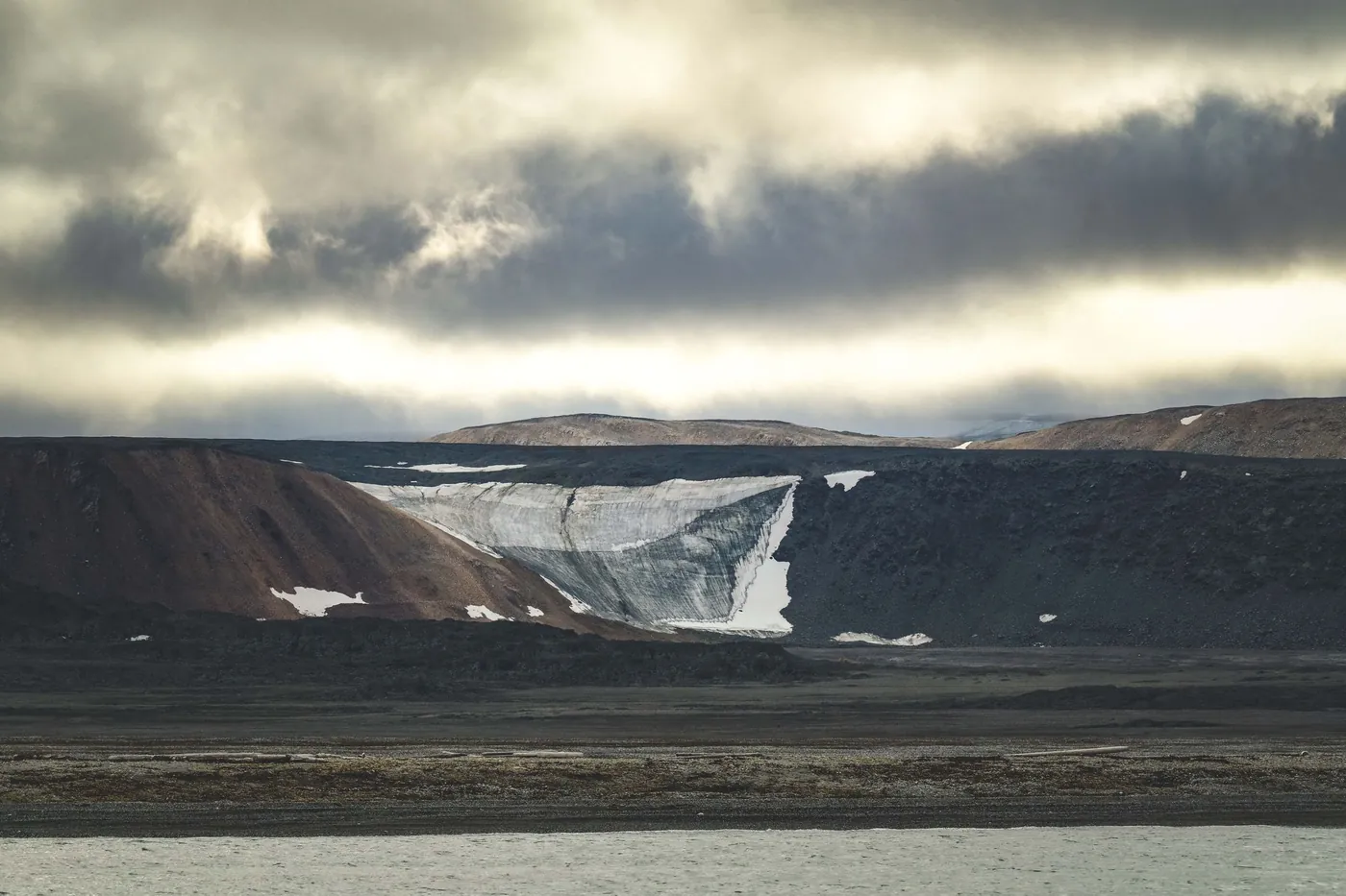 Montañas de meseta desnudas con un pequeño glaciar bajo densas nubes de verano