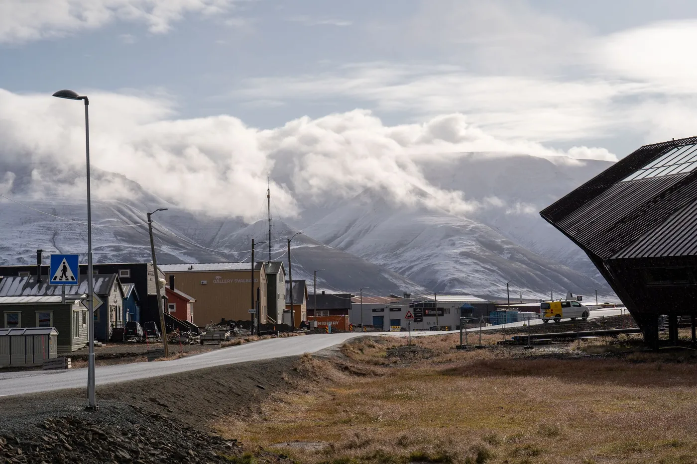 Road leading through Longyearbyen past low houses toward cloud-covered mountains