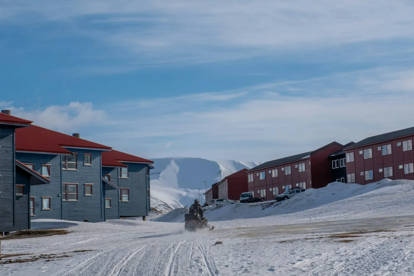 Snowmobile driving along a snowy track between red and grey houses