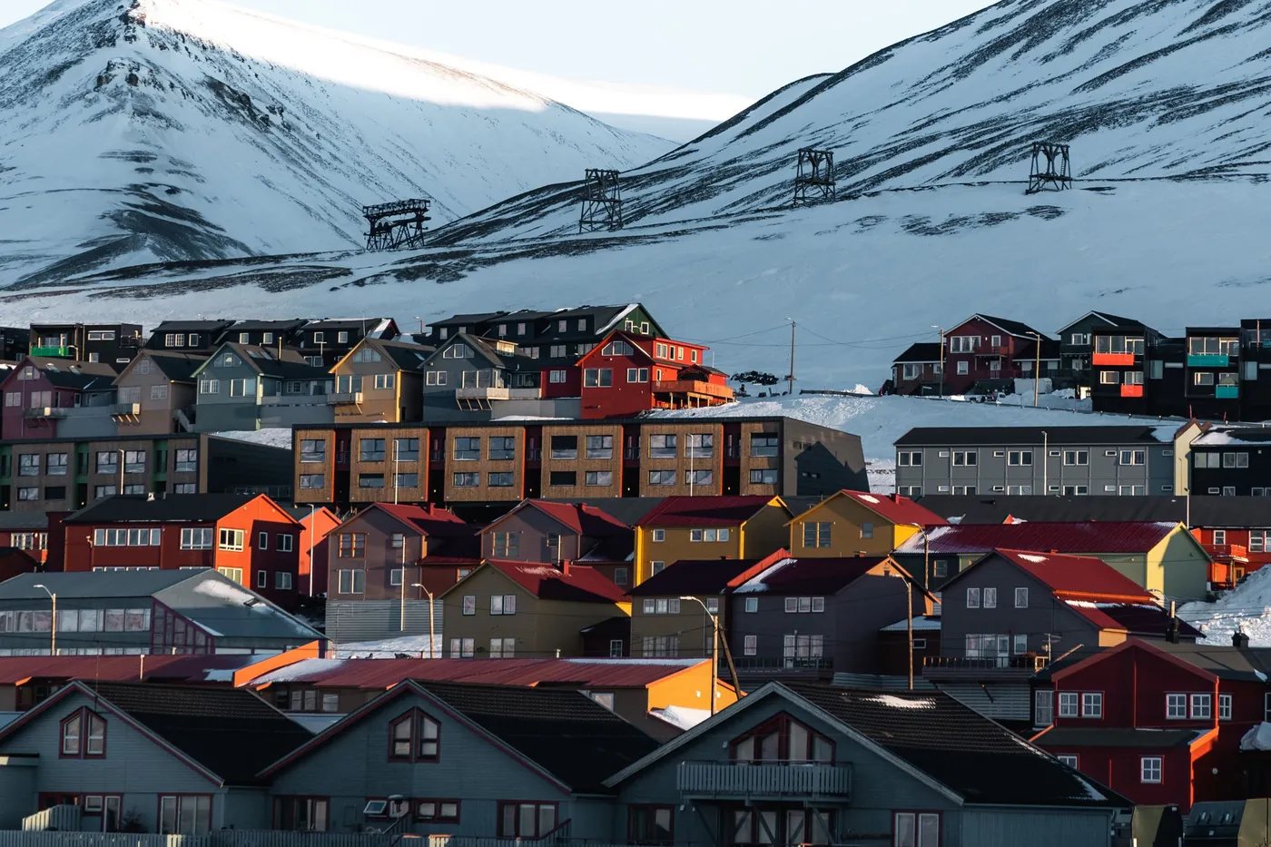 Casas de madera de colores bajo montañas nevadas con antiguas torres de teleférico