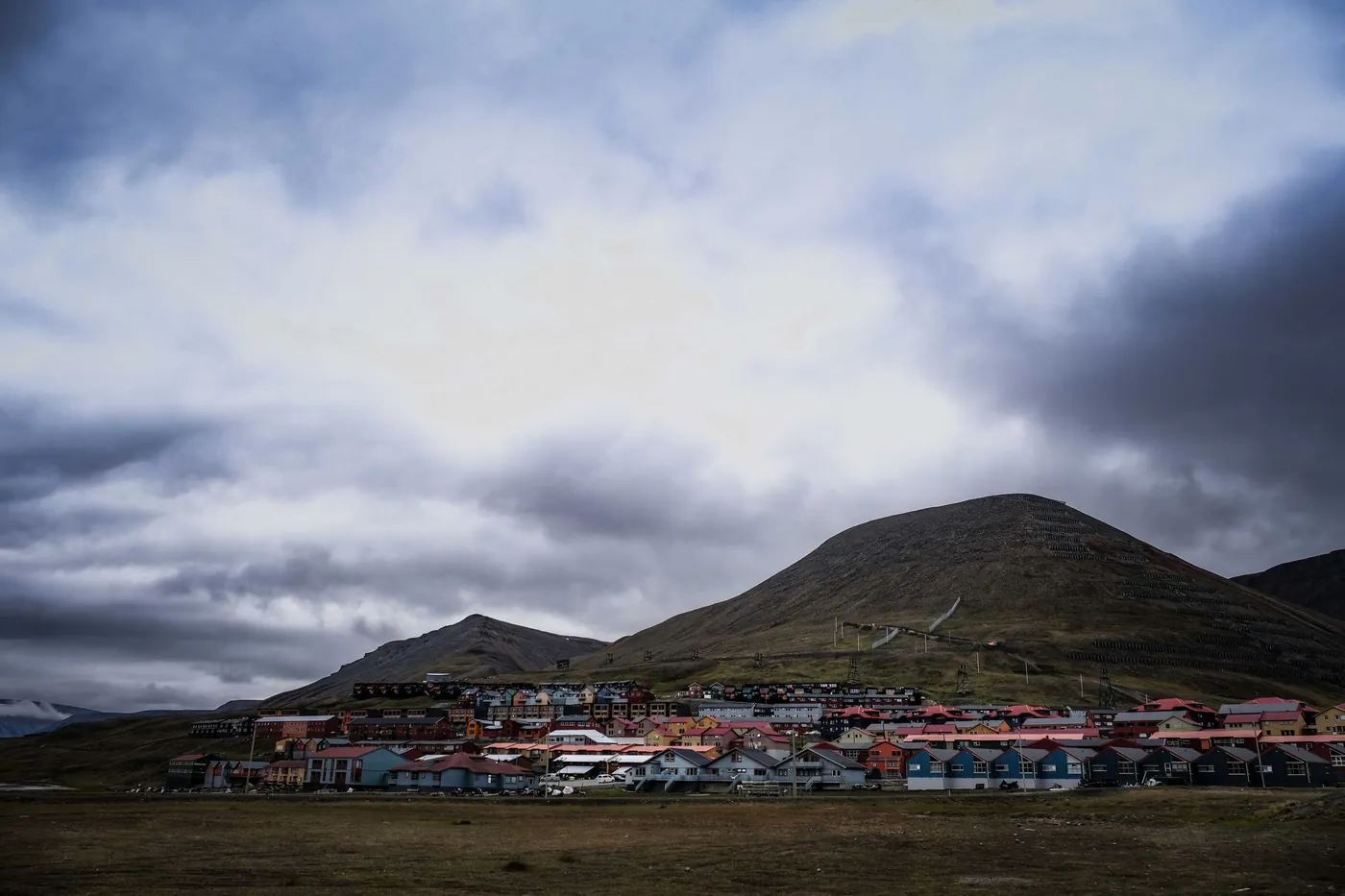 Row of colourful houses at the foot of a green hill under dramatic clouds